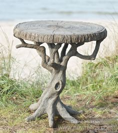 a tree stump table sitting on top of a grass covered field next to the ocean