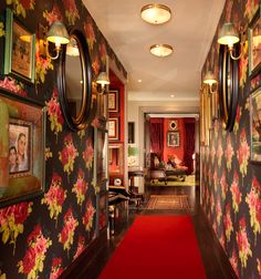 the hallway is decorated with floral wallpaper and framed pictures on the walls, along with a red carpet