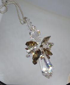 a clear crystal flower pendant hangs from a silver chain on a white surface with light shining in the background