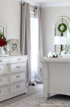 a white dresser sitting next to a bed in a bedroom under a window with curtains