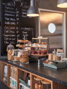 an assortment of pastries and desserts on display at a cafe counter in front of a chalkboard