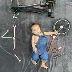 a baby is laying on the ground next to tools, including a wrench and screwdrivers