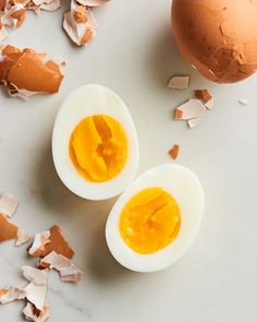 two hard boiled eggs on a white surface with broken egg shells around them and an egg yolk in the middle