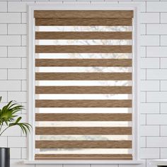 a white brick wall with a window covered in shades of brown and white striped blinds