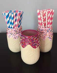 two mason jars with pink and blue striped straws in them, one is filled with sprinkles