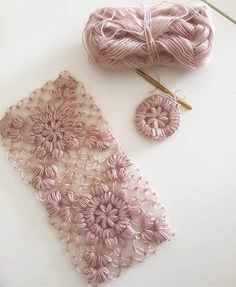 two balls of yarn and some crochet on a white table with pink flowers