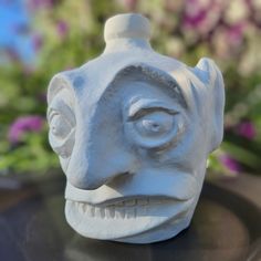 a white ceramic mask sitting on top of a table next to some purple and pink flowers