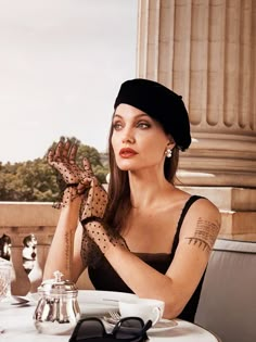 a woman sitting at a table with her hands in the air while wearing gloves and a hat