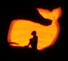 the silhouette of a person sitting in front of a carved pumpkin shaped like a dog