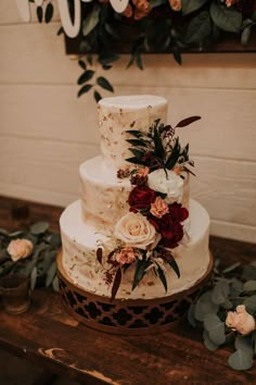 a three tiered wedding cake with flowers and greenery sits on a wooden table