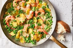 a skillet filled with shrimp, potatoes and peas next to a piece of bread