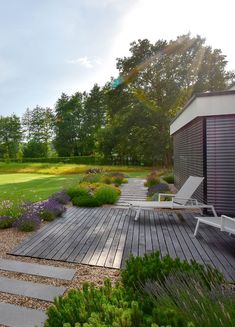 a wooden deck in the middle of a grassy area with flowers and trees around it