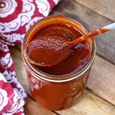 a jar filled with sauce sitting on top of a wooden table next to a red and white towel