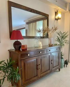 a large mirror sitting on top of a wooden cabinet next to a lamp and potted plant