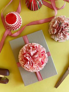 some paper flowers are sitting on top of a piece of gray and red material next to a pair of scissors