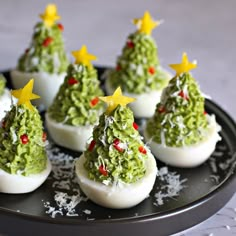 deviled eggs decorated as christmas trees on a black plate with shredded cheese sprinkles