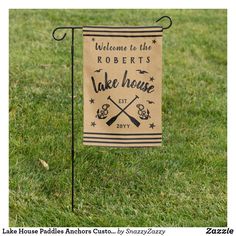 a garden flag that says welcome to the robert's lake house with crossed paddles on it