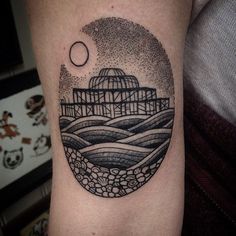 a black and white photo of a circular tattoo on the arm with an image of a building