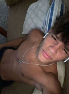 a shirtless man laying on top of a bed wearing headphones in his ears