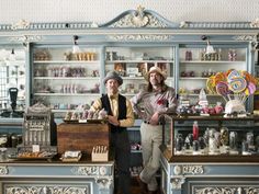 two men standing in front of a display case filled with candies and lollipops