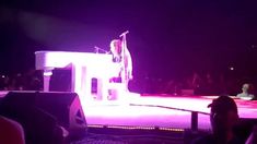 a man standing on top of a white piano in front of a crowd at night