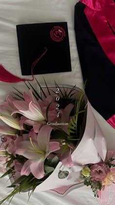 a bouquet of pink flowers sitting on top of a bed next to a graduation cap