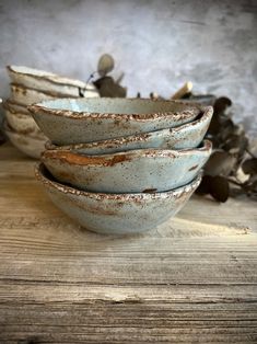 a stack of ceramic bowls sitting on top of a wooden table next to dried leaves