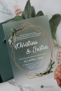 a person holding up a wedding card with greenery on it