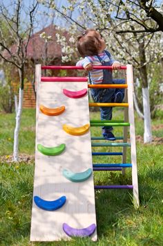 a toddler playing on an outdoor wooden climbing frame in the grass with trees behind him