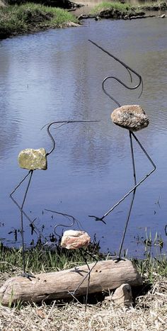 three metal sculptures sitting on top of a grass covered field next to a body of water