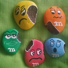 four rocks with faces painted on them sitting next to each other in front of a green cloth