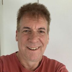 an older man with short hair smiling for the camera while wearing a red t - shirt