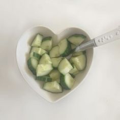 a heart shaped bowl filled with cucumbers next to a knife on top of a table