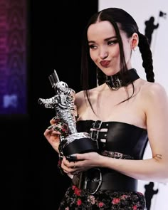 a woman in a black dress holding a silver trophy and looking at the camera while standing on stage