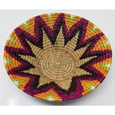 a woven basket with an orange, yellow and purple design on the bottom is sitting on a white surface