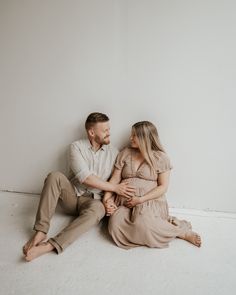 a man and woman sitting on the floor next to each other in front of a white wall