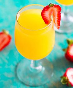 two glasses filled with orange juice and strawberries on a blue tablecloth next to each other