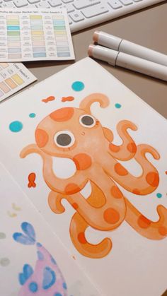 an orange octopus is sitting on the table next to a keyboard and paper with watercolors