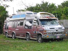 an old bus is parked in the grass next to a fence with trees and bushes behind it