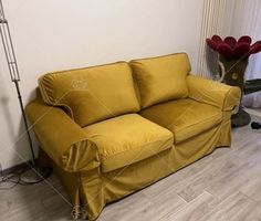 a yellow couch sitting on top of a hard wood floor next to a vase with flowers