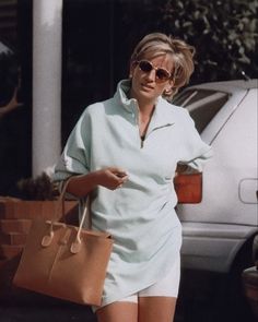 a woman walking down the street carrying a brown purse and wearing white shorts with her hand on her hip