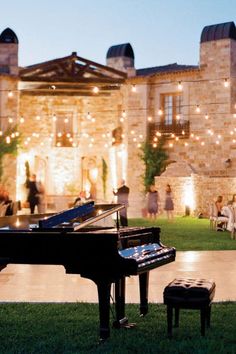 a grand piano sitting in front of a large building with string lights strung around it