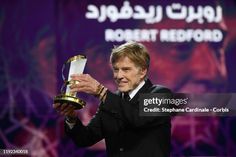 an older man holding up a trophy in front of a purple and black background with arabic writing