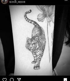 a black and white photo of a tiger on someone's arm with flowers in the background