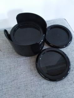 three black dishes sitting next to each other on top of a gray carpeted floor