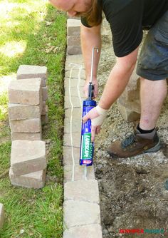 Putting construction adhesive on bricks to make a retaining wall How To Build A Brick Retaining Wall, Diy Landscaping Edging, Paver Retaining Wall Raised Beds, Building A Retaining Wall Flower Bed, Retaining Wall How To, Retaining Walls Driveway, Pavers Retaining Wall, Retaining Wall Along Driveway, Diy Flowerbed Edging