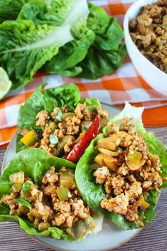 lettuce wraps filled with meat and vegetables on a plate next to a bowl of salad