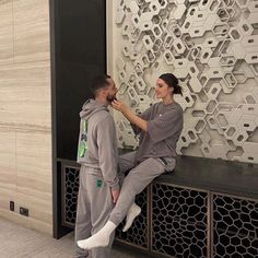 a man and woman standing next to each other in front of a wall with geometric designs