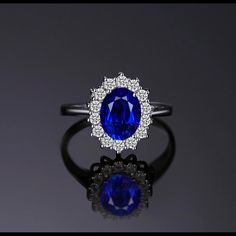 an oval shaped blue and white diamond ring on top of a black surface with the center stone surrounded by smaller round diamonds