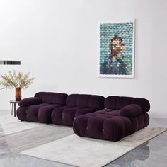 a large purple couch sitting on top of a white rug in a living room next to a painting